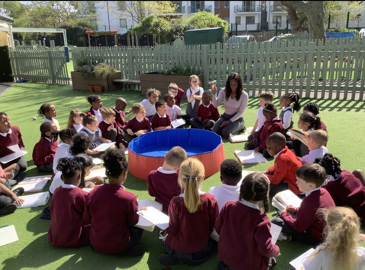 A group of children sitting in a circle with their teacher outside
